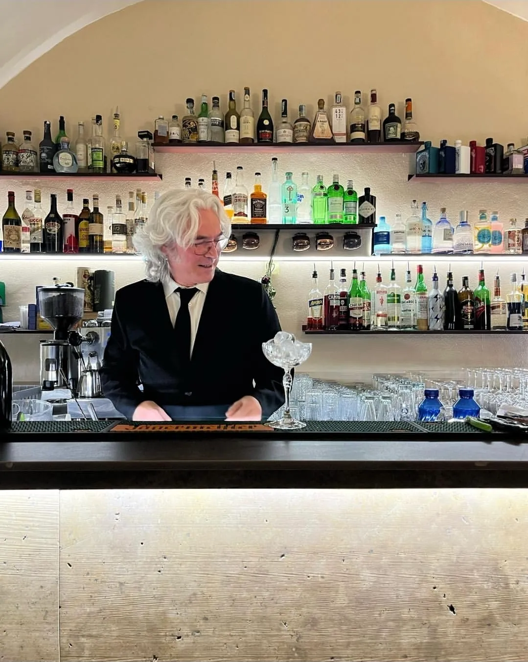 Il barman dietro al bancone con la parete dei distillati
