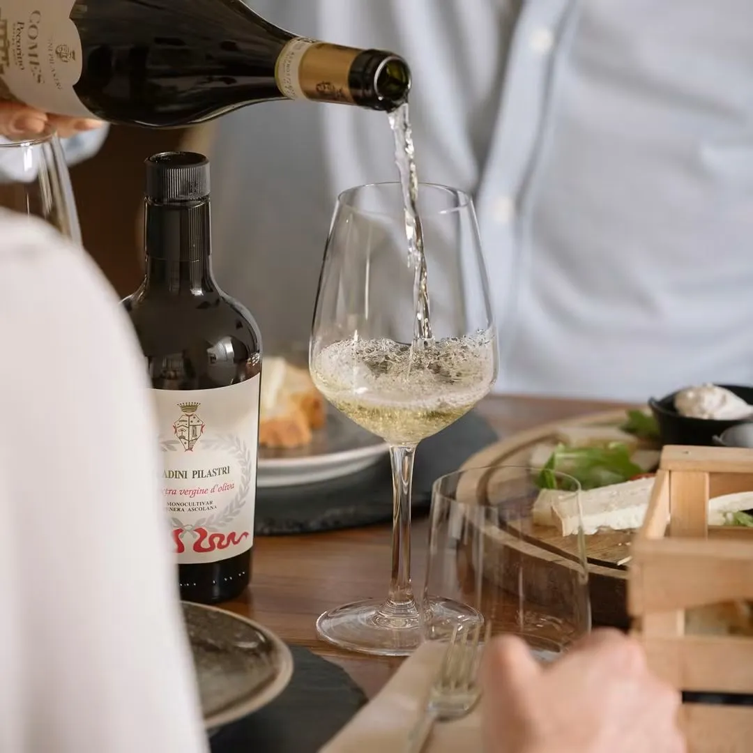 Vino bianco versato nel calice accanto all'olio monocultivar Tenera Ascolana